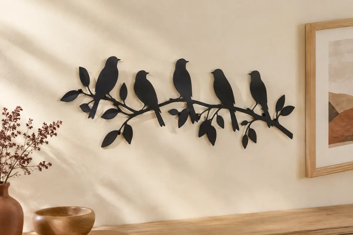 Sculpture murale noire en métal représentant cinq oiseaux sur une branche, posée sur un mur crème.